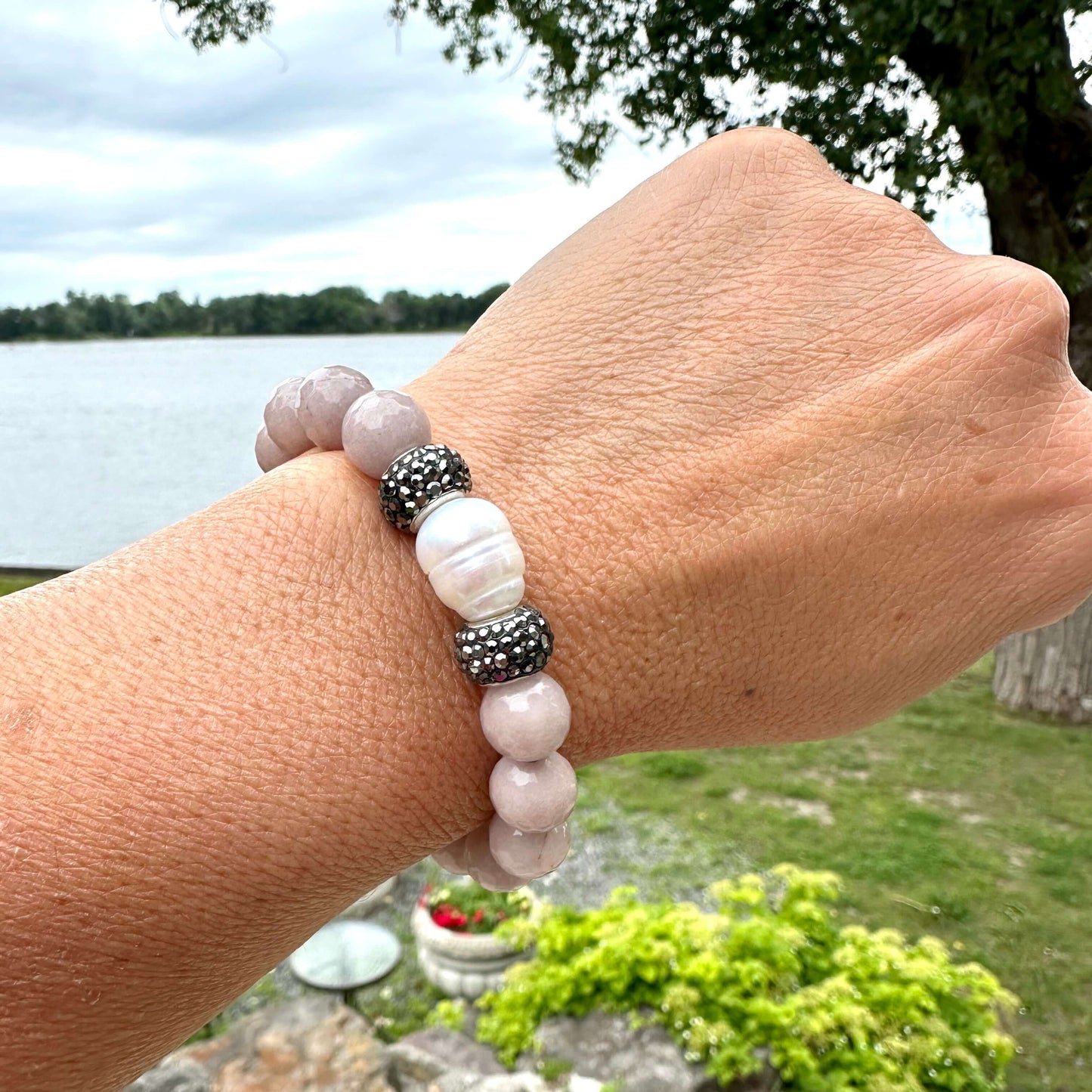 Pink jade pearl bracelet worn on female wrist by lake and greenery