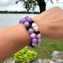 Load image into Gallery viewer, Two lavender jade bracelets worn together on a woman’s wrist near flowers
