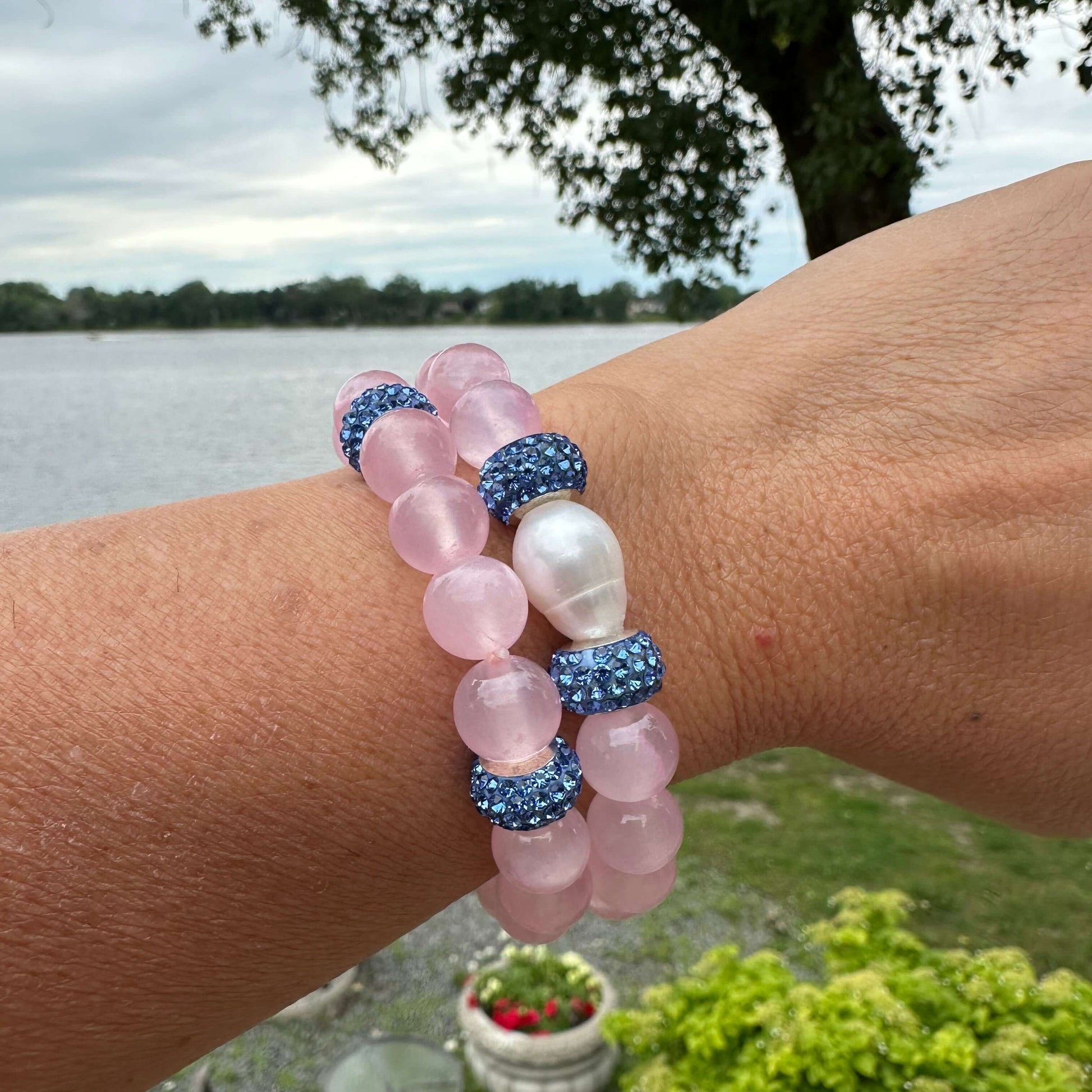Pink jade bracelet with freshwater pearl and rhinestone accents worn on wrist by lake.