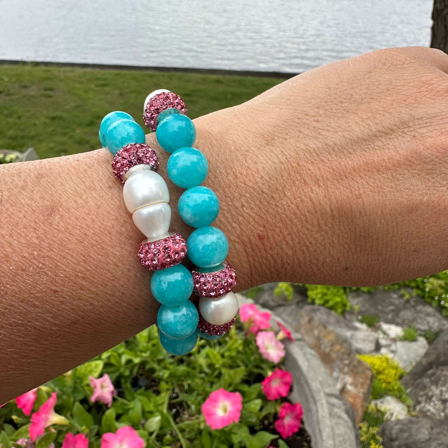 Teal jade bracelet with pearls and pink accents showcased on a wrist by a scenic waterfront.