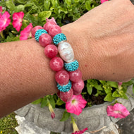 Two red jade bracelets with blue rhinestones, one with a pearl, worn on a woman’s wrist