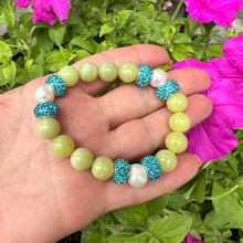 Load image into Gallery viewer, Olive green jade bracelet with three pearls held in hand near pink flowers
