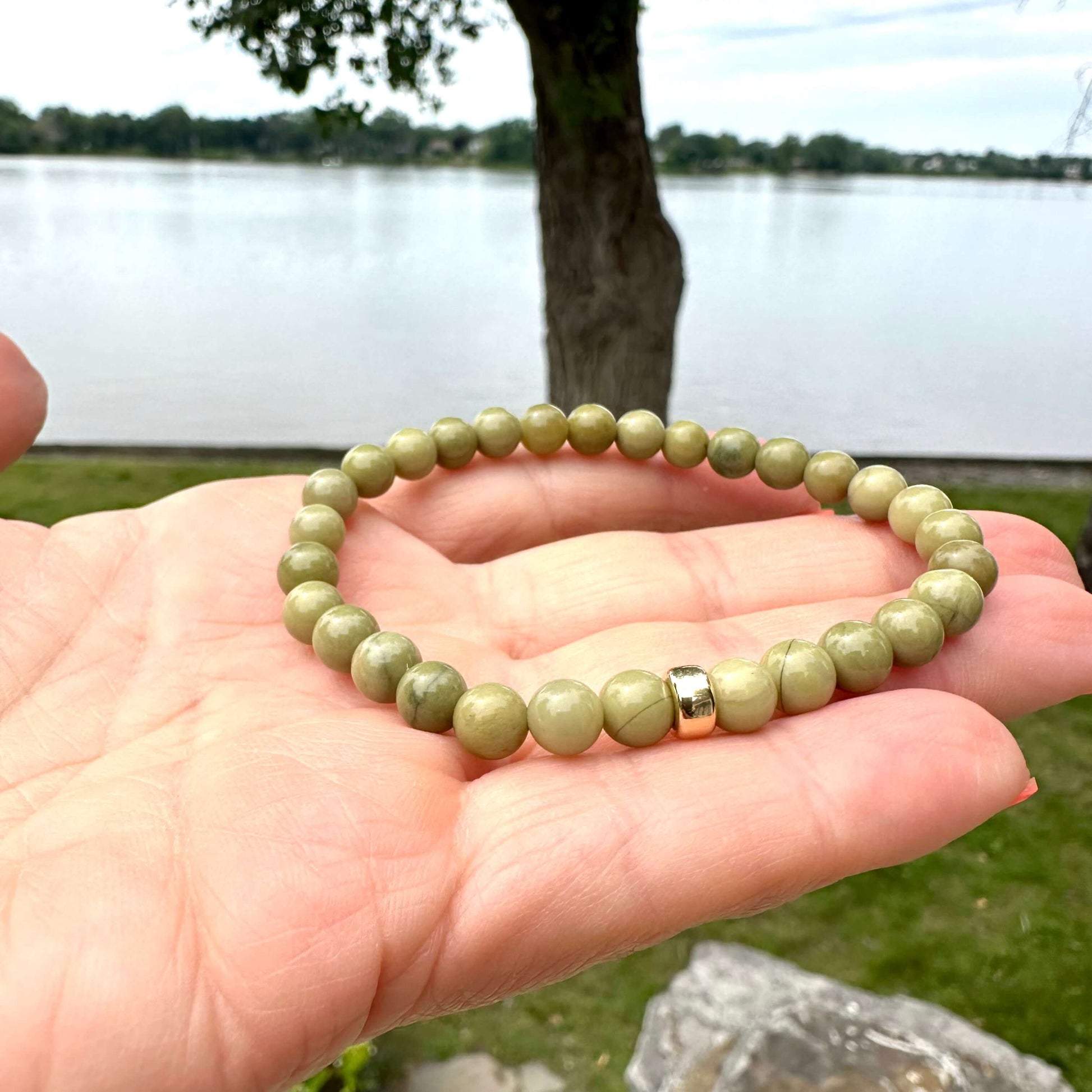 olive green jasper bracelet displayed on hand against scenic lake background.