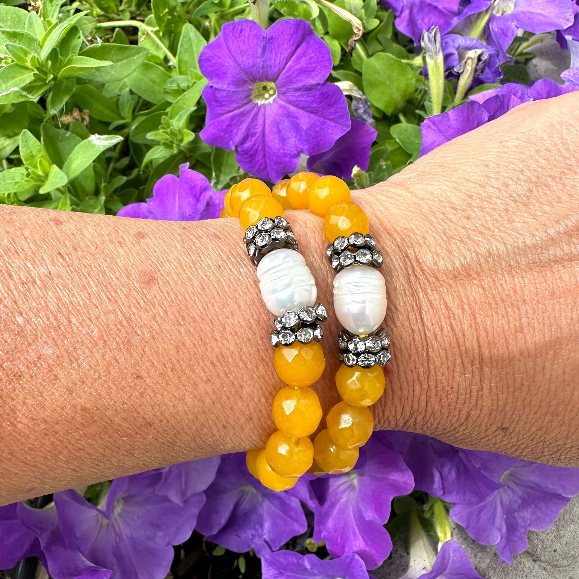 Yellow jade pearl bracelet showcased on wrist against a backdrop of purple flowers, featuring vibrant yellow jade beads and freshwater pearl.