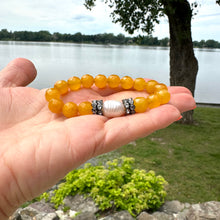 Load image into Gallery viewer, Yellow jade pearl bracelet held in hand near natural lake
