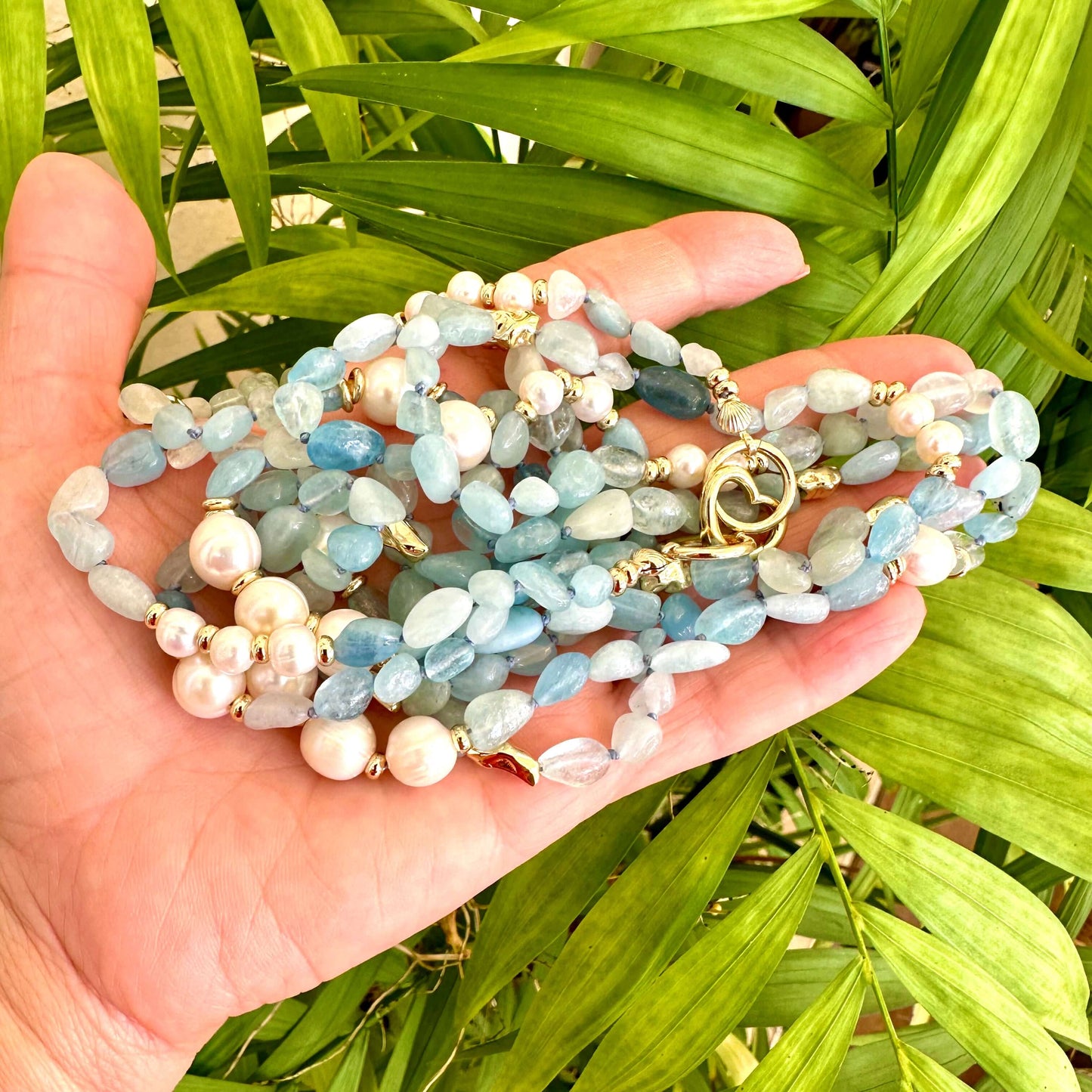 Aquamarine and pearl necklace held in hand against green foliage