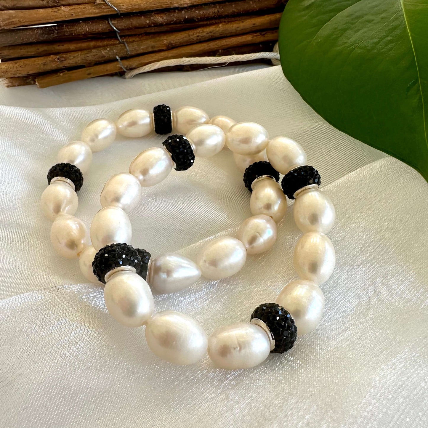 Close-up of white pearl stretch bracelet with black rhinestones on white fabric