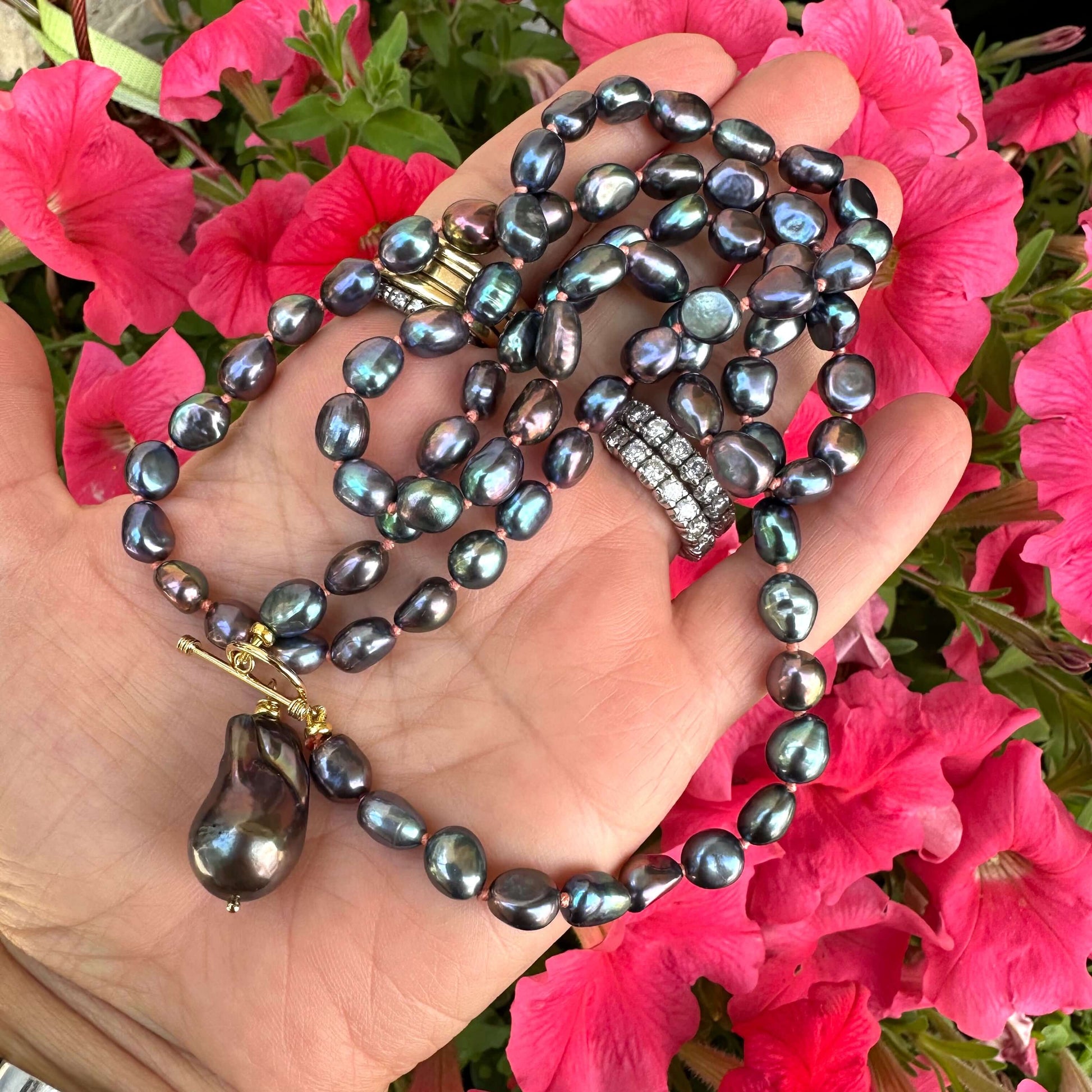 Close-up of peacock black pearl necklace with baroque pendant held outdoors near foliage