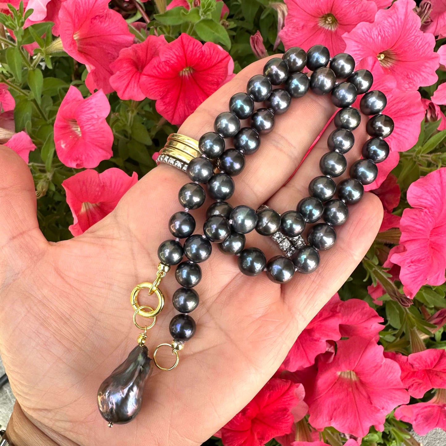 Black pearl necklace with baroque pendant held in hand near flowers