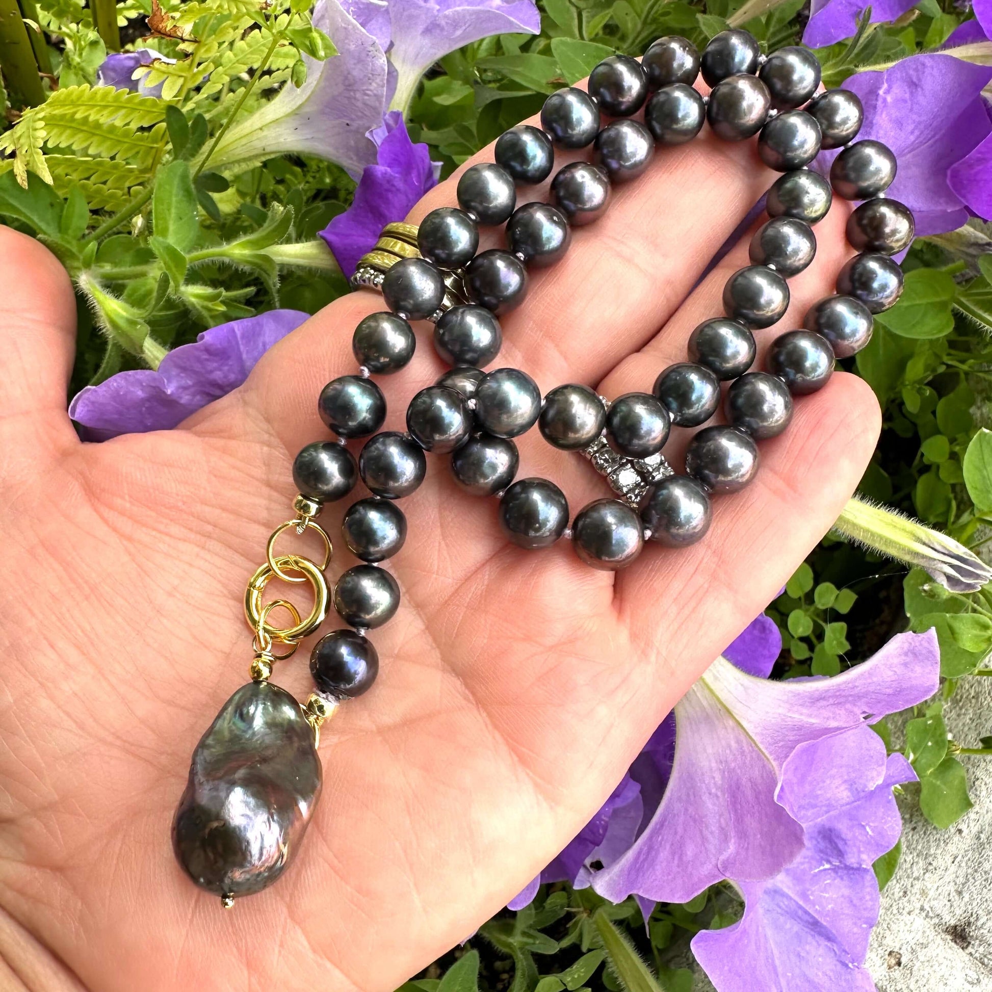 Close-up of black pearl necklace with removable pendant held in hand against floral background