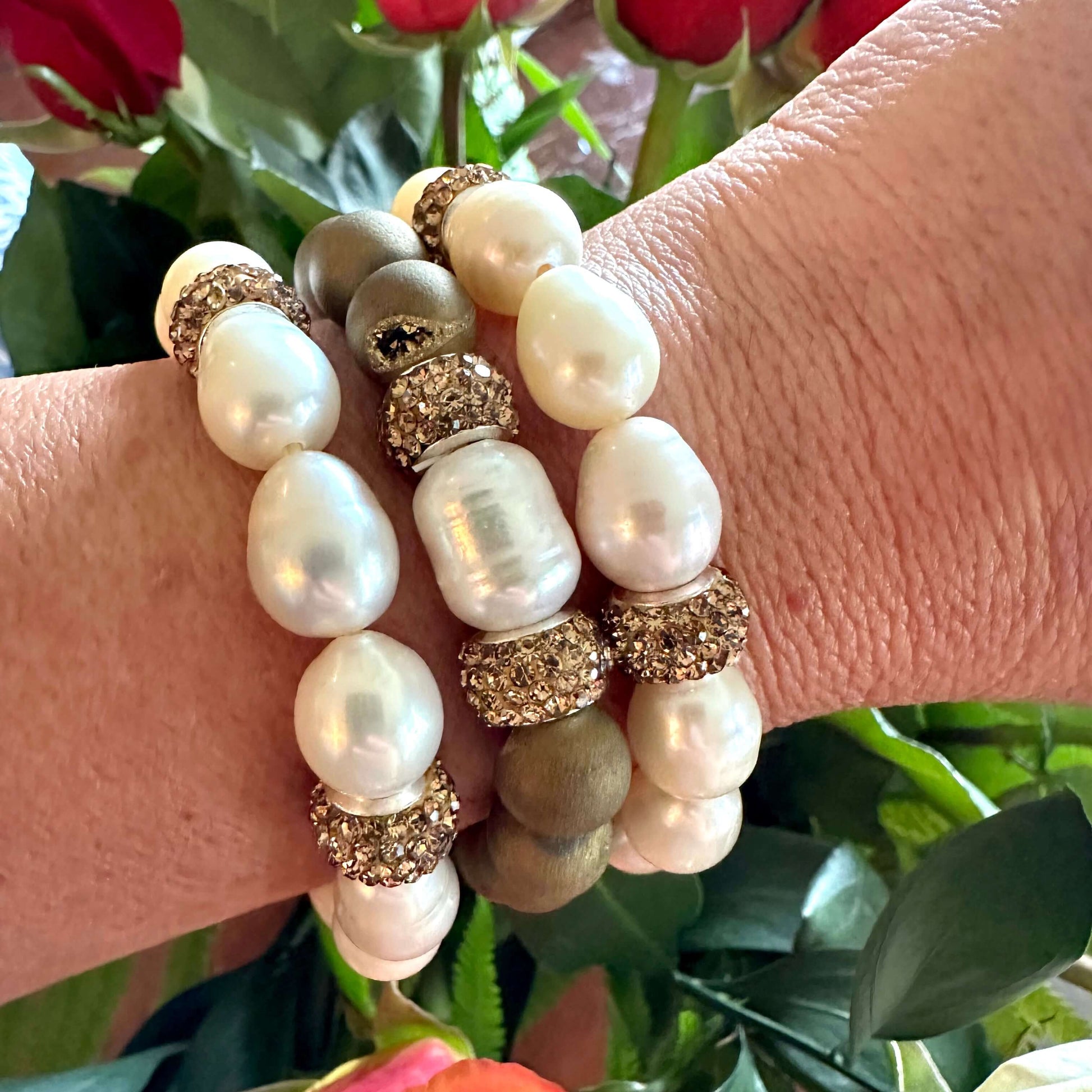 White pearl stretch bracelets with golden rhinestones worn on wrist near flowers