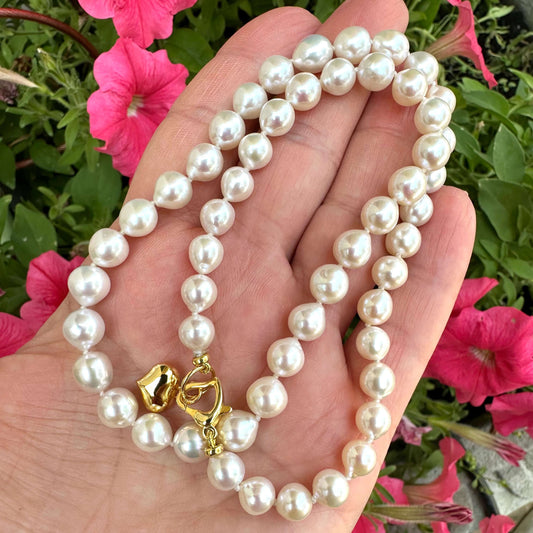 Classic pearl necklace with gold heart charm beautifully displayed in hand among vibrant pink flowers.