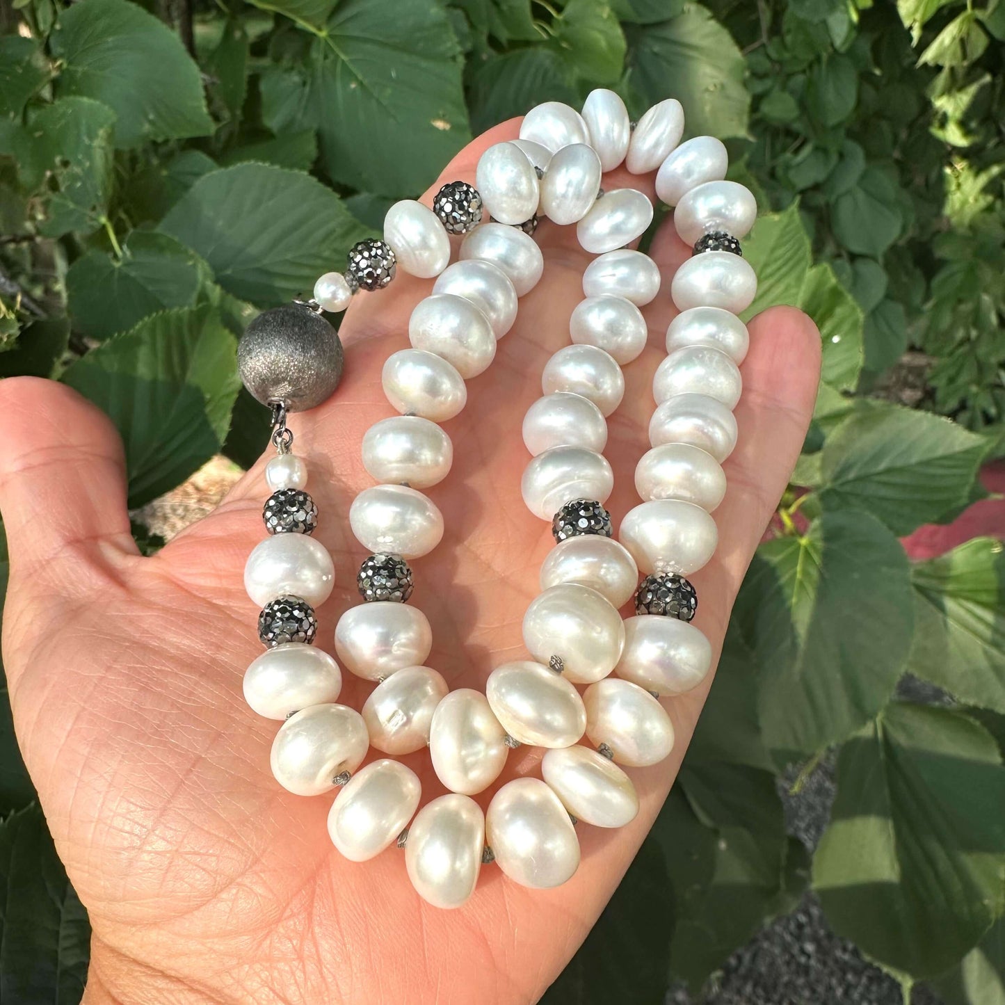 White button pearl necklace with rhinestone beads held in hand against green foliage