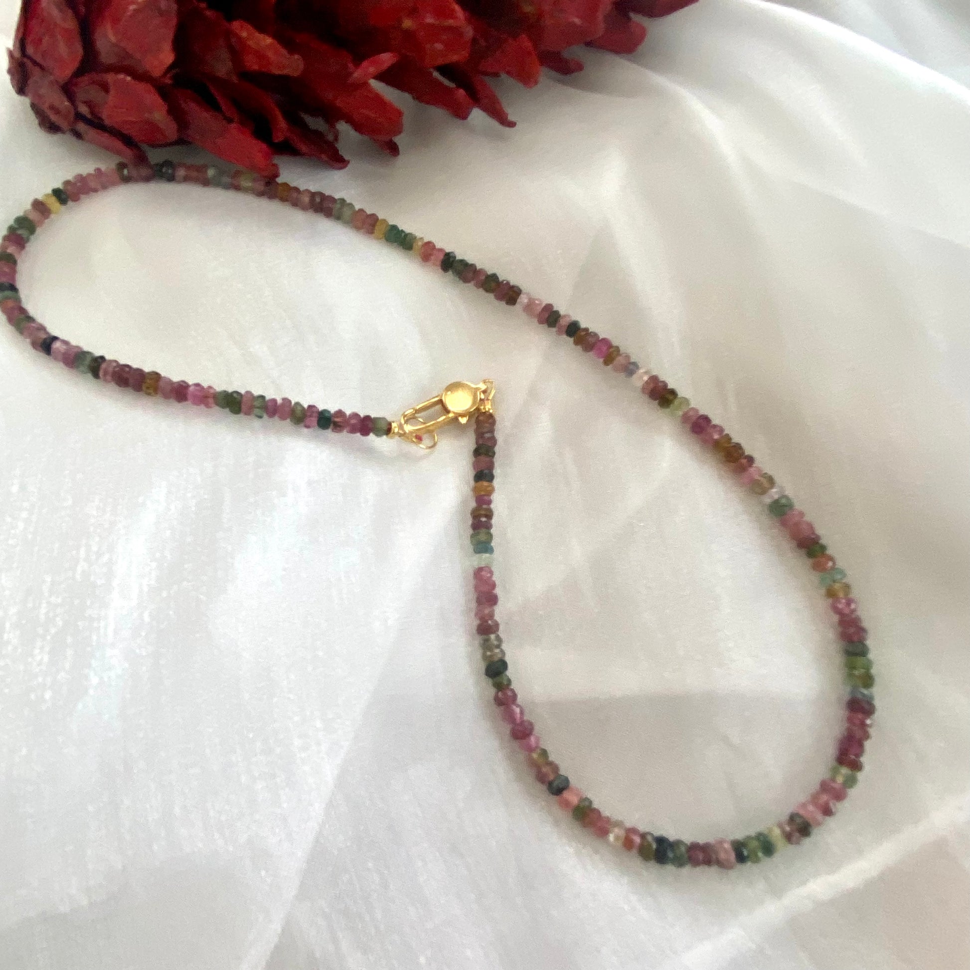 Watermelon tourmaline necklace laid on white cloth, close-up detail
