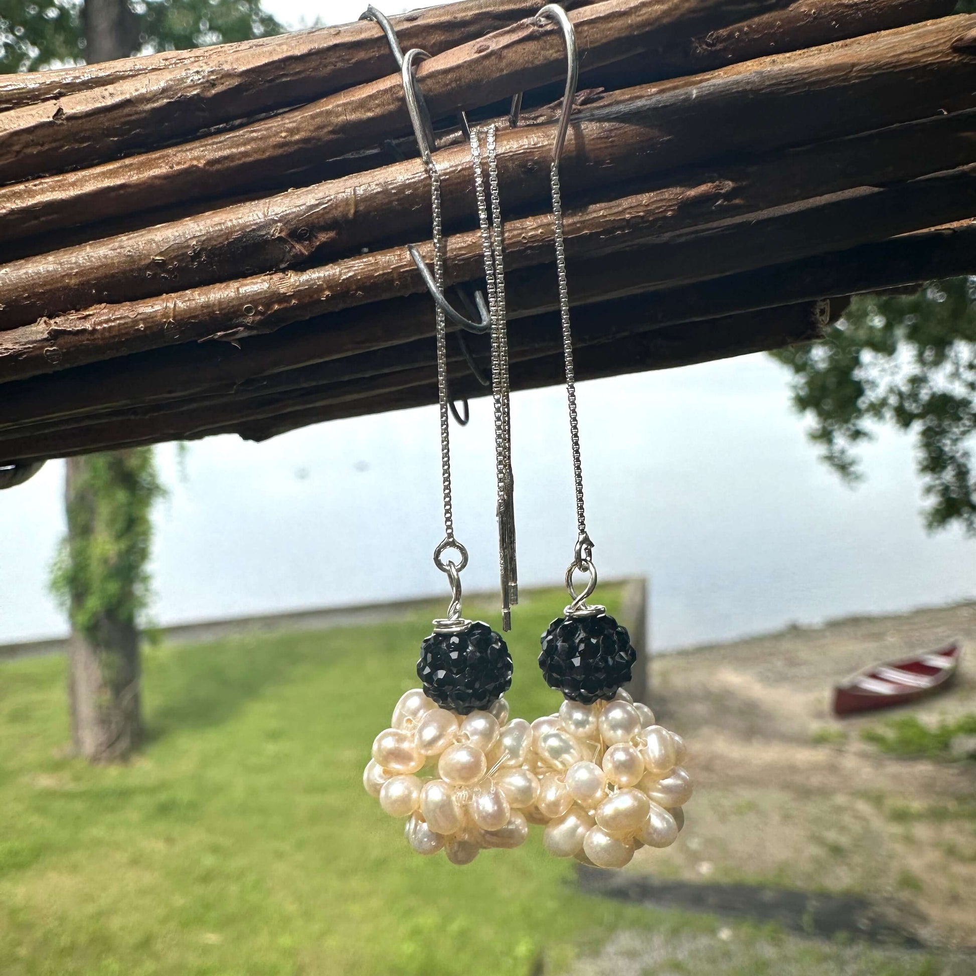 White pearl threader earrings with black rhinestones dangling from a branch with lake in background