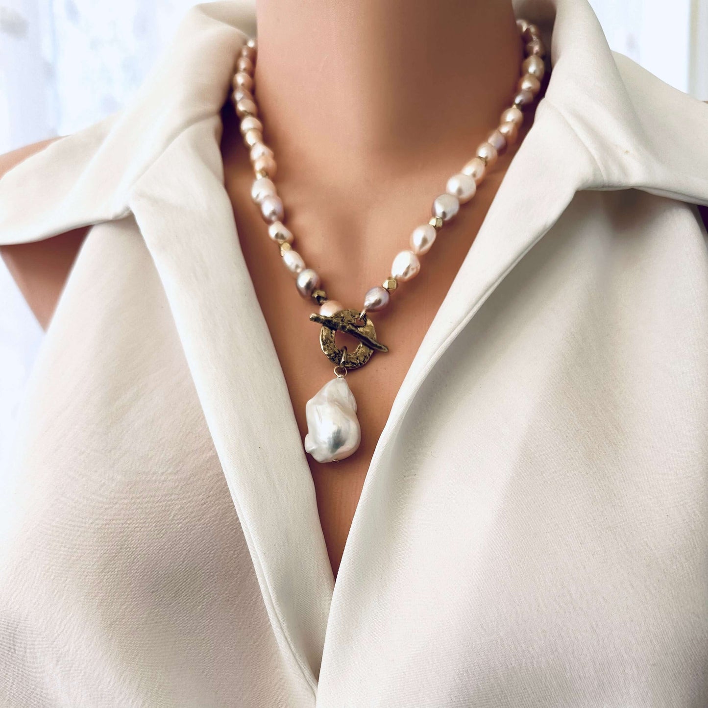 Side close-up of pastel pearl necklace worn by mannequin showing baroque pearl pendant