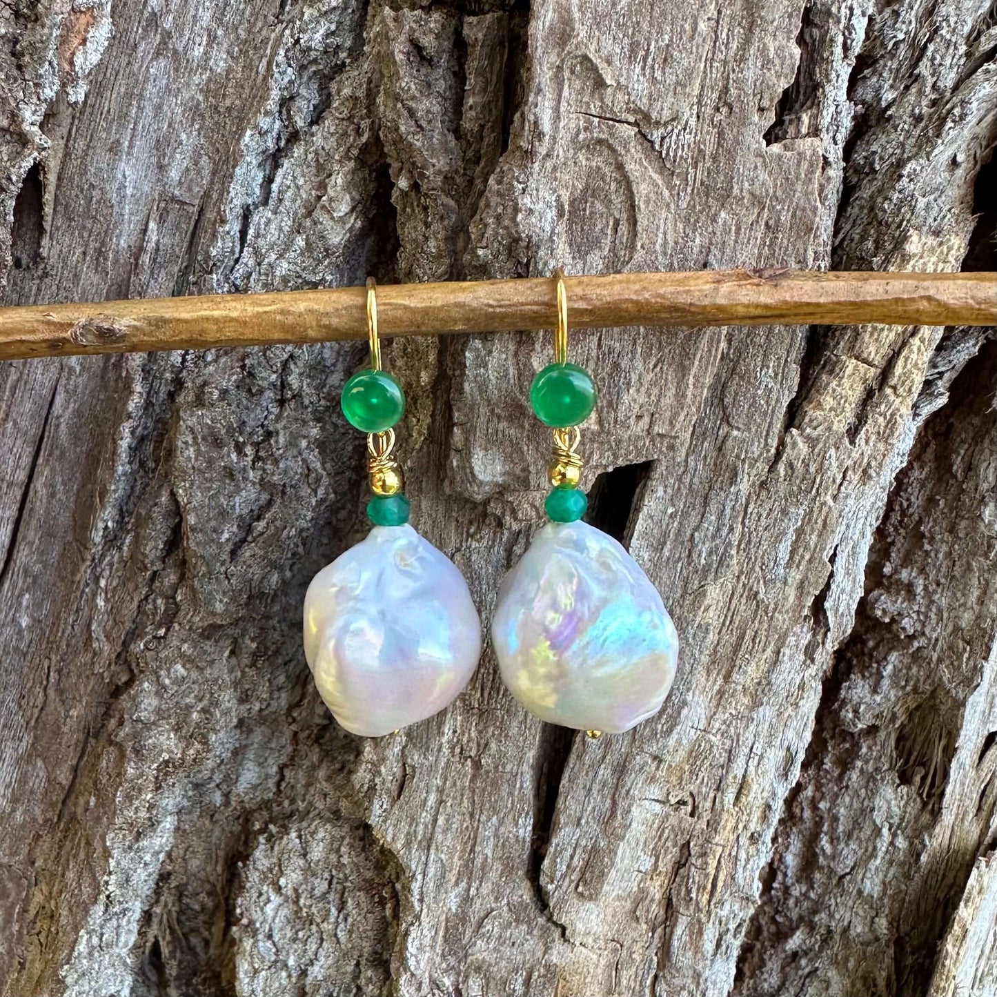 White baroque pearl drop earrings with green agate on a wooden background, showcasing unique shape and elegance.