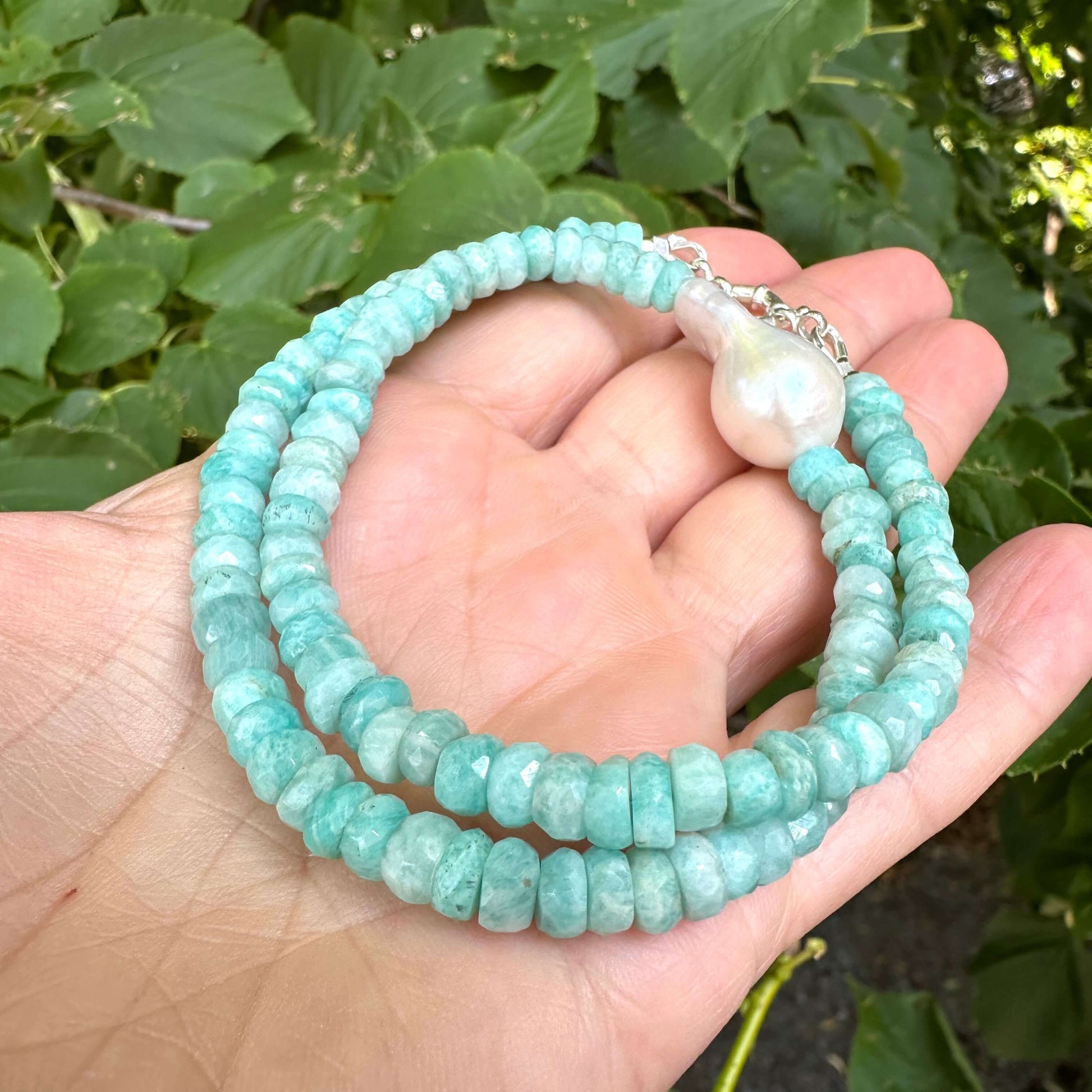 Close-up of amazonite and white baroque pearl necklace held in hand showing gemstone color variations