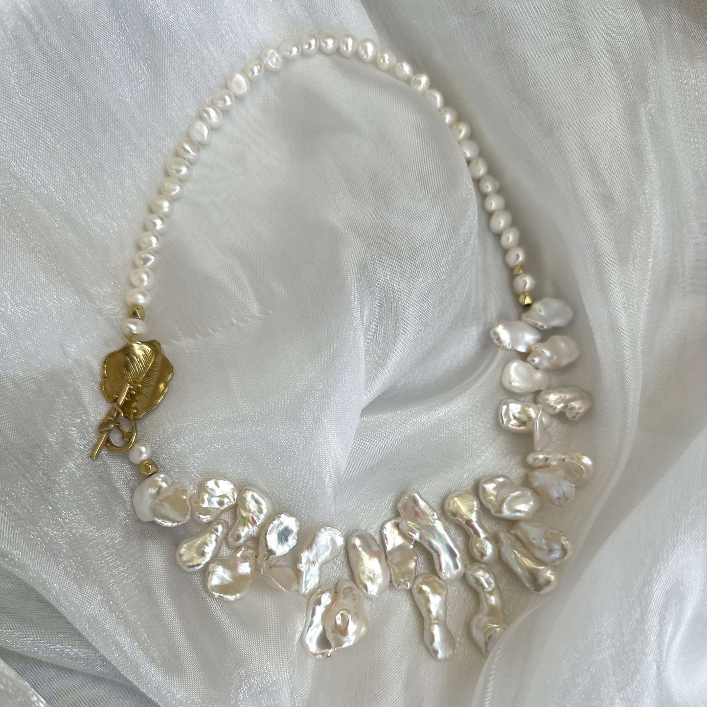 Close-up of white petal pearl necklace on white fabric highlighting asymmetrical pearls