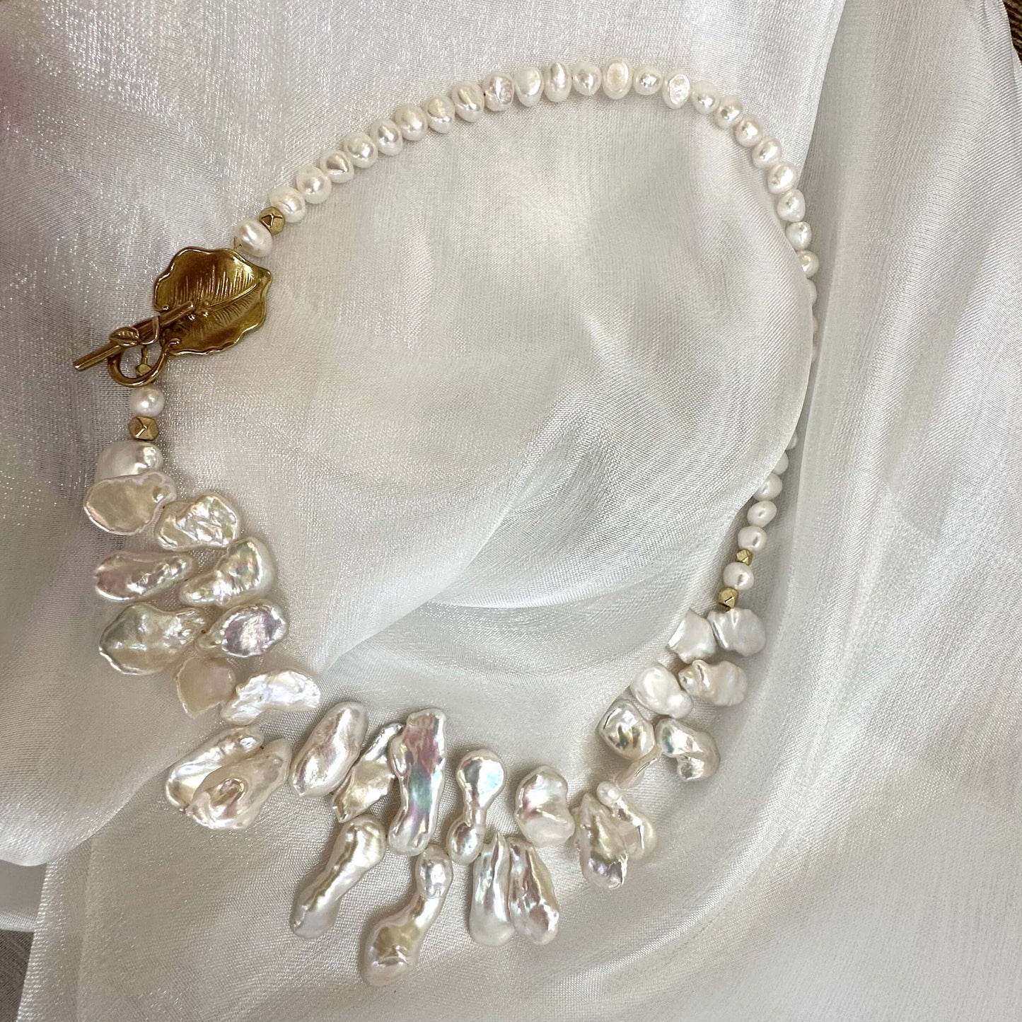 White petal pearl necklace displayed on white cloth background showing golden leaf clasp