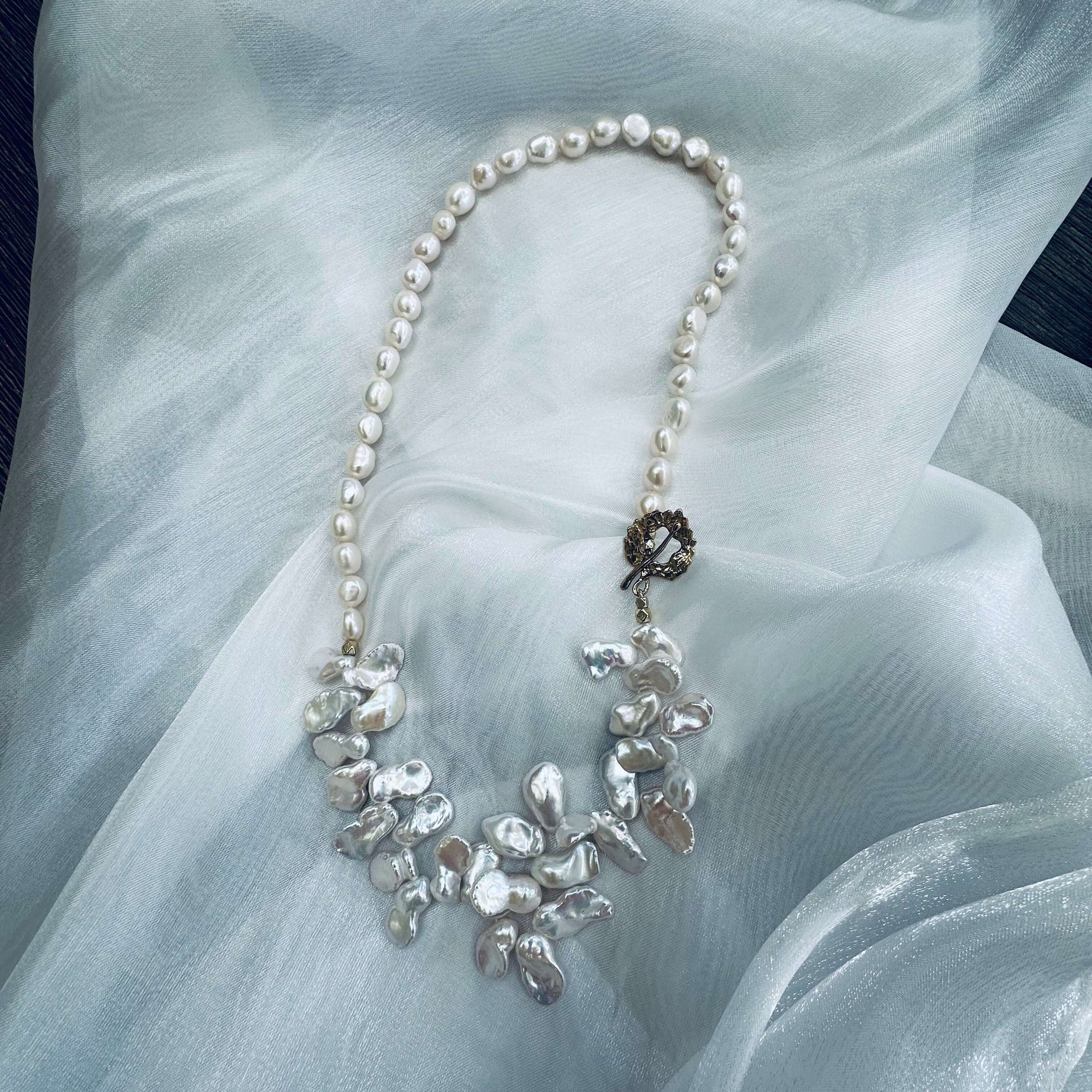 White keshi pearl necklace displayed on white cloth table showing nugget and petal pearls