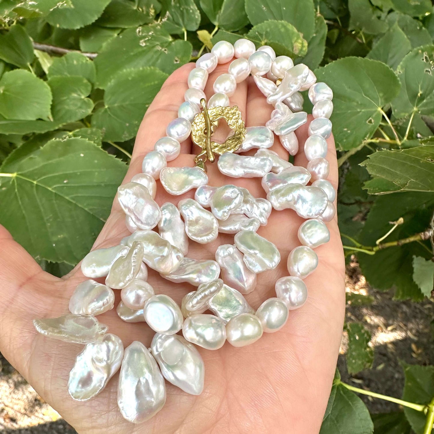 White keshi pearl necklace held in hand with green foliage background showing iridescent luster