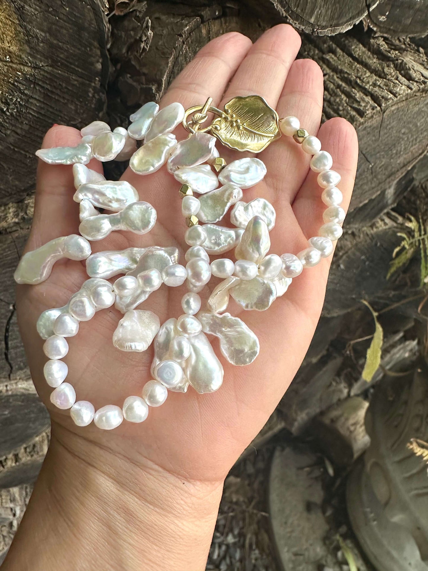 White petal pearl necklace held in hand against wood logs backdrop showing natural luster