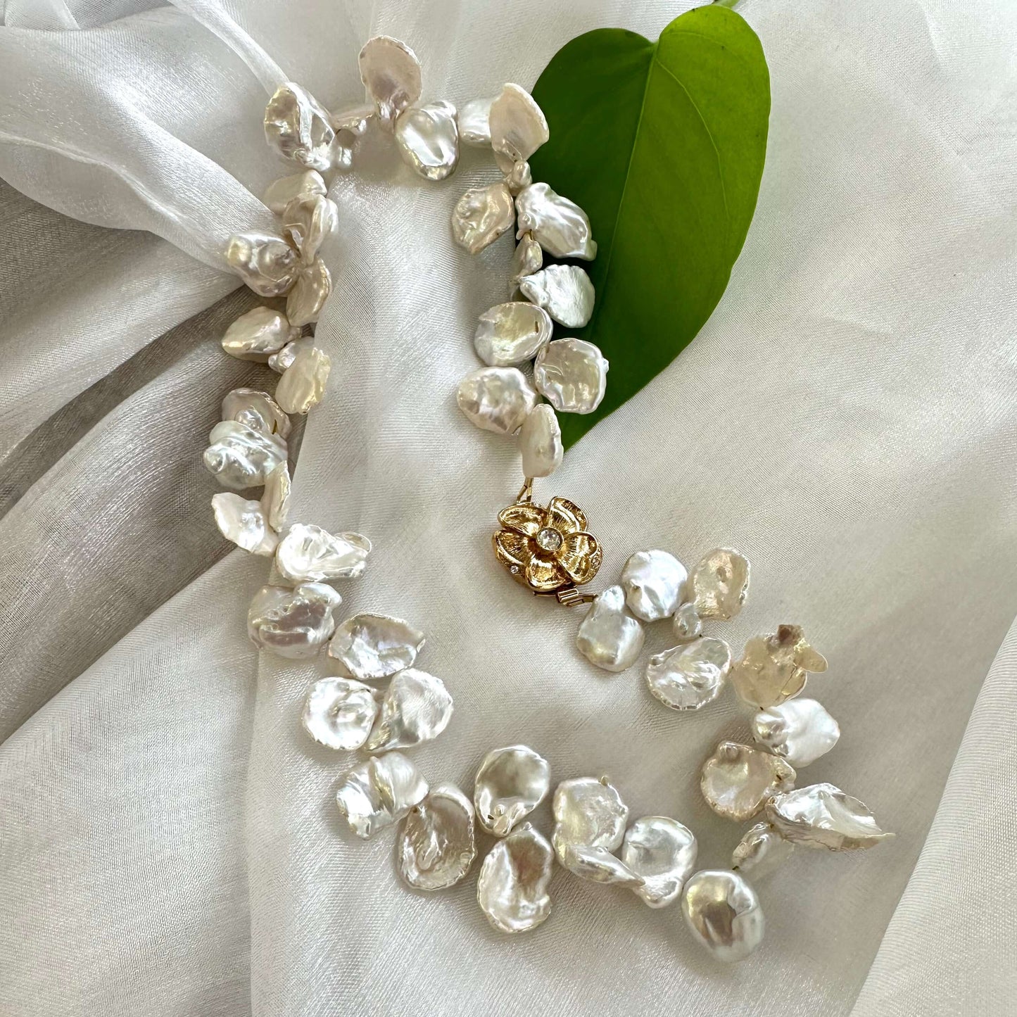 Close-up of white keshi pearl necklace with flower clasp on white fabric showing iridescent luster