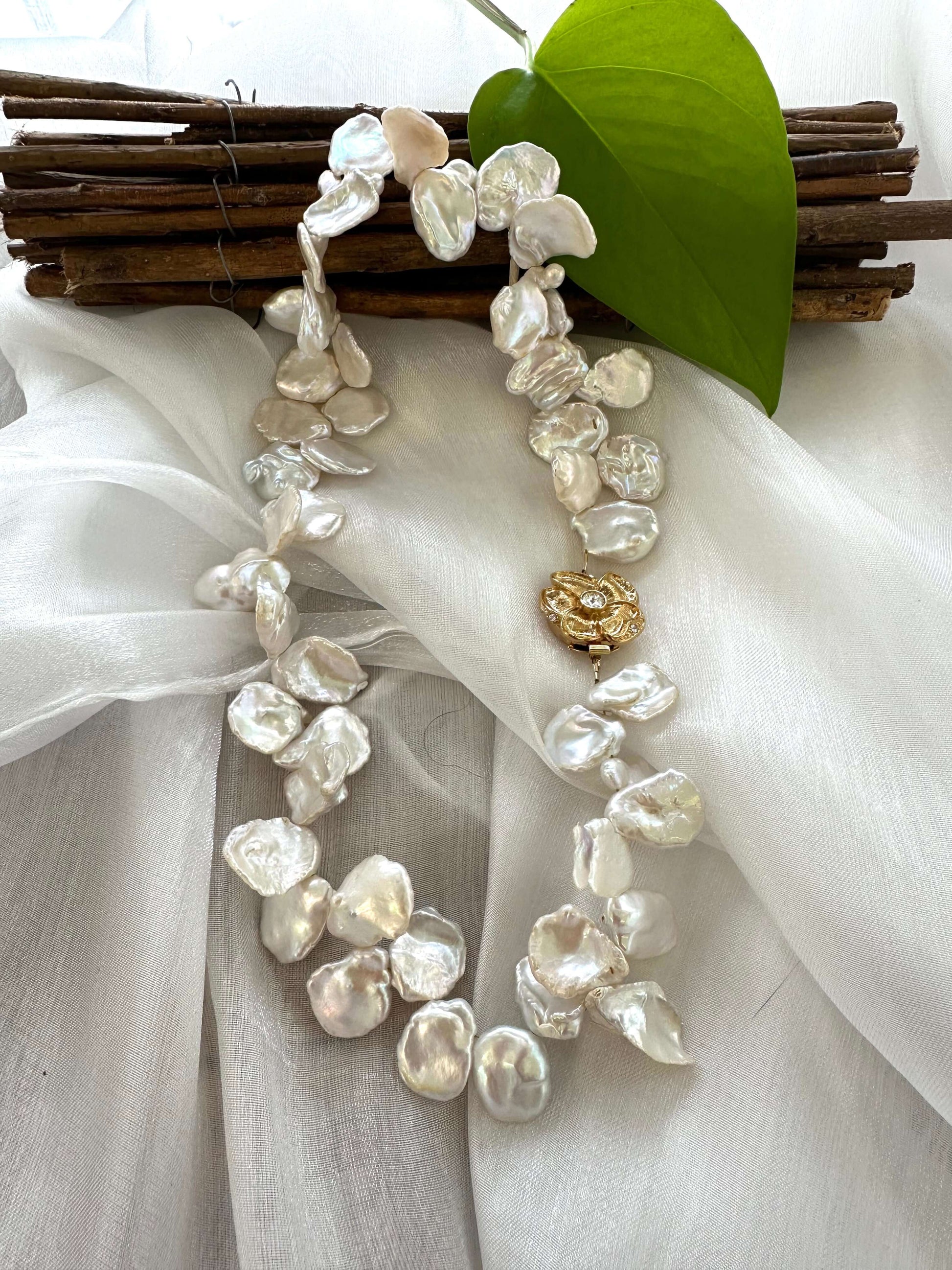White keshi pearl necklace with flower clasp displayed on white cloth table, detailed view of pearls