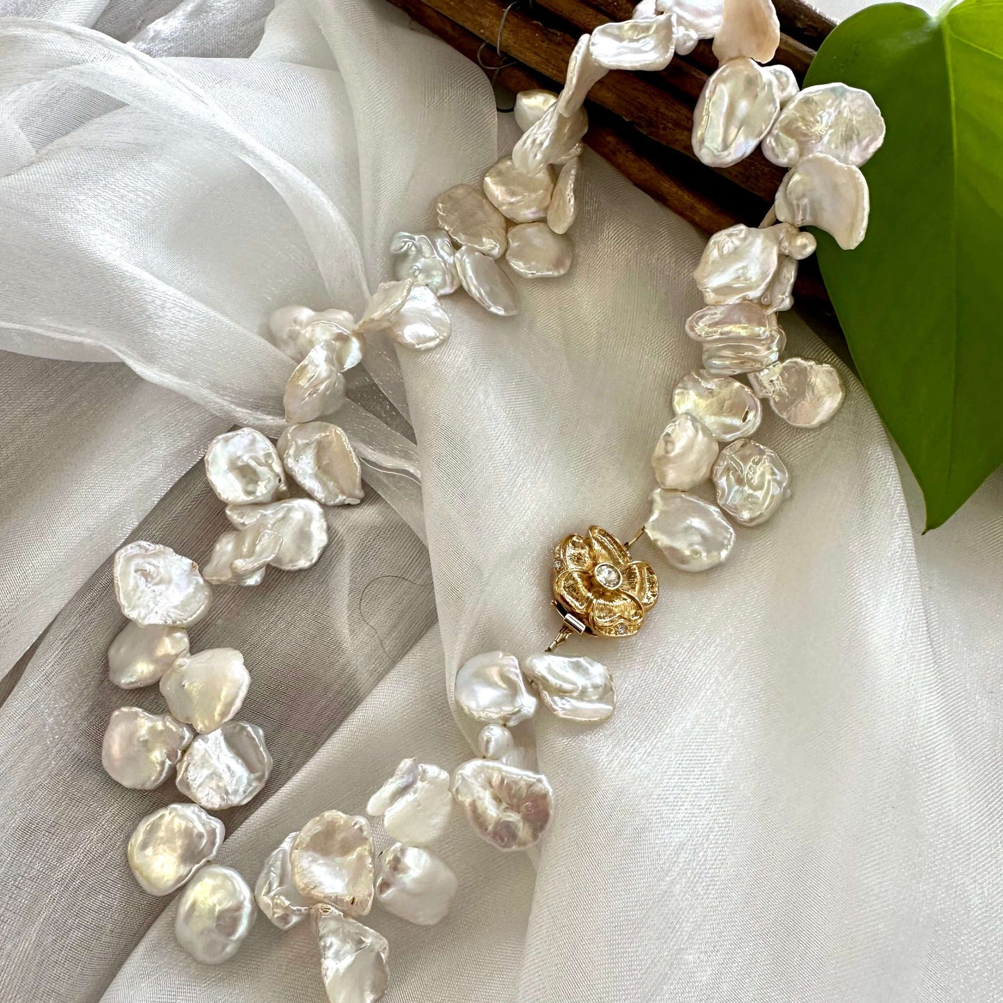 White keshi pearl necklace with flower clasp arranged on white cloth for product photography