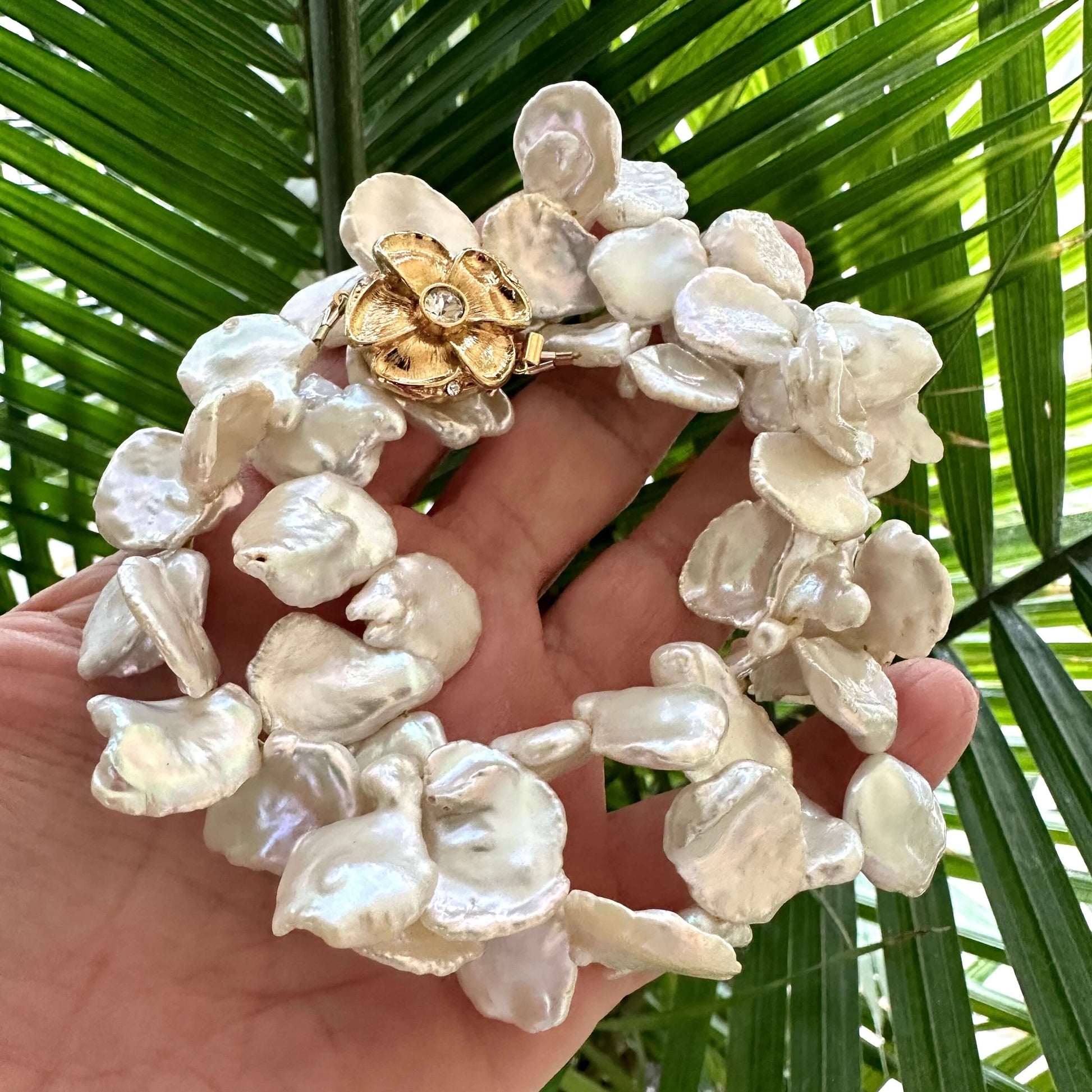 White keshi pearl necklace with flower clasp held in hand against green foliage background