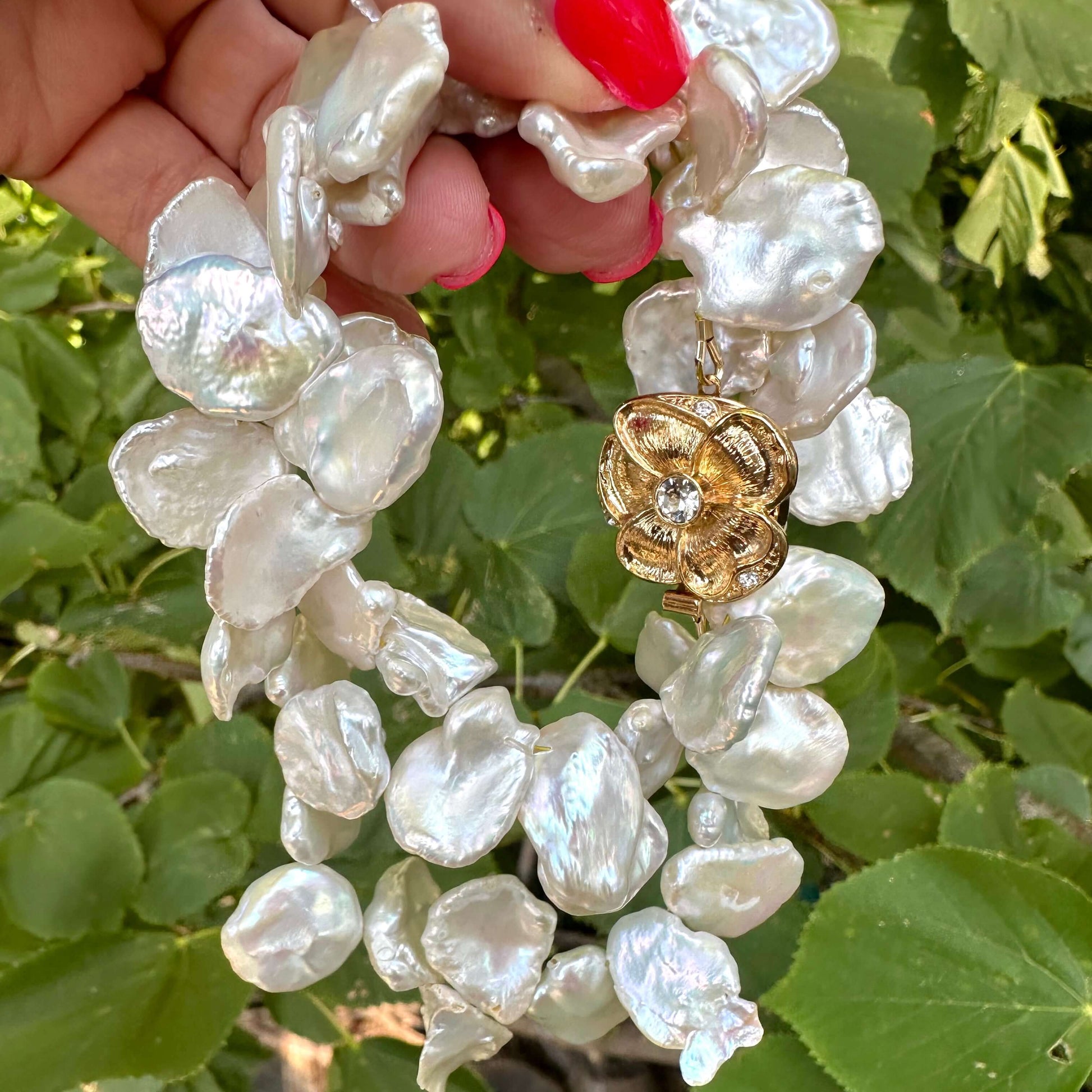 Close-up of white keshi pearl necklace with flower clasp in natural light with greenery backdrop
