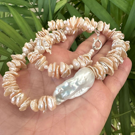 Close-up of peach keshi pearl necklace with baroque pearl held near green foliage