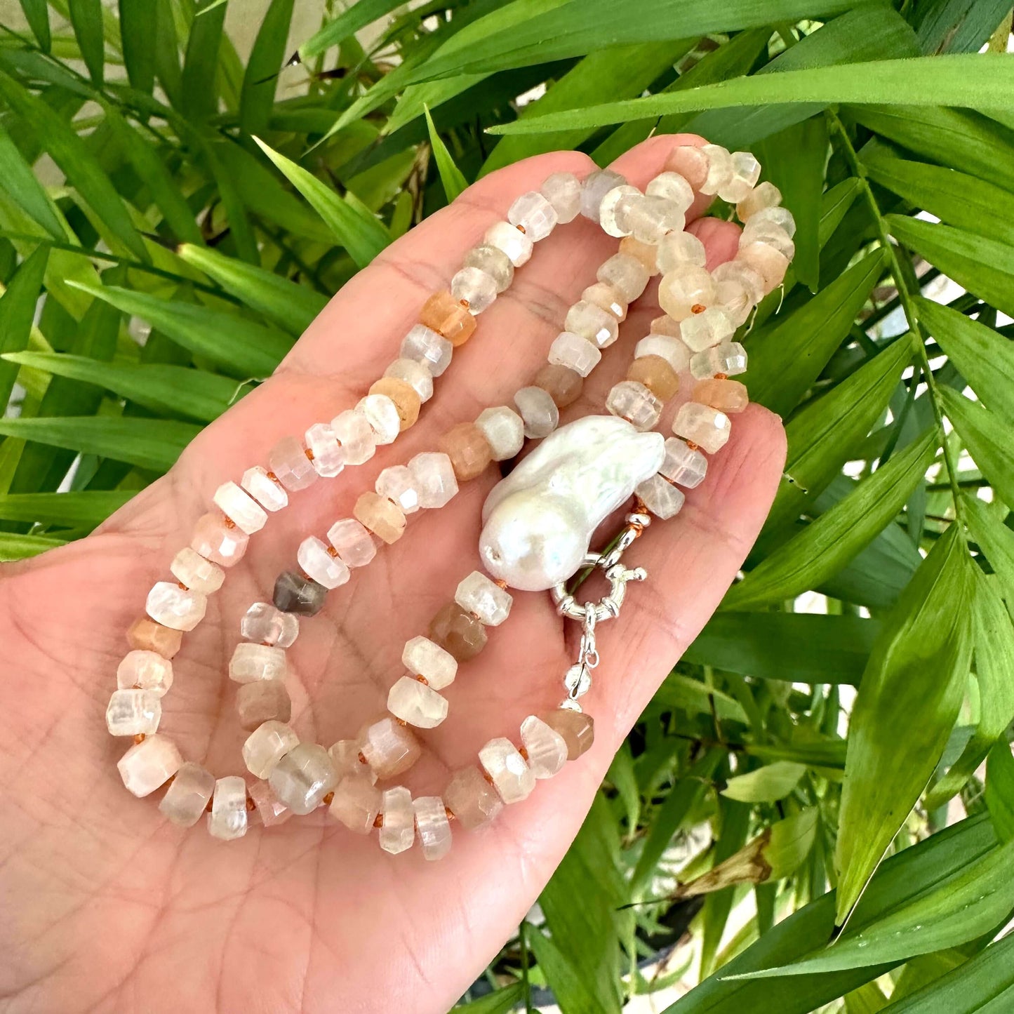 Close-up of mixed moonstone and baroque pearl necklace held in hand against green foliage