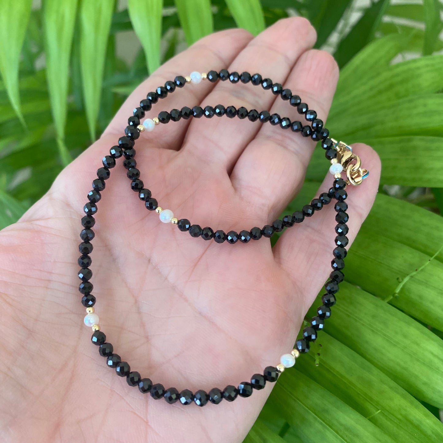 Black spinel pearl choker necklace held in hand against green foliage