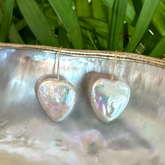 Heart shape freshwater pearl drop earrings displayed on a shell, showcasing their lustrous sheen and handmade craftsmanship.
