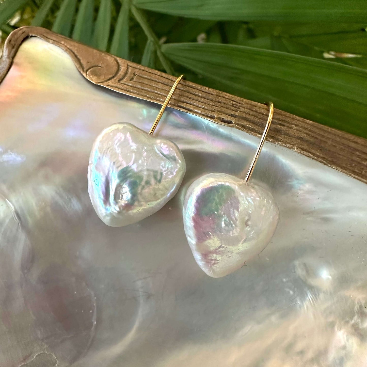 Heart shape freshwater pearl drop earrings displayed on a natural shell background, showcasing their lustrous shine.