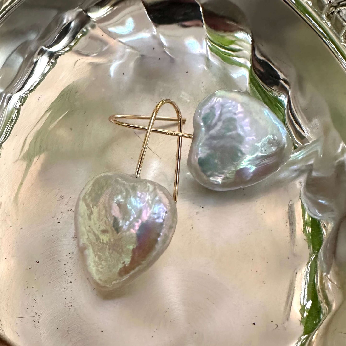 Heart shape freshwater pearl drop earrings on a silver dish, showcasing their natural luster and handmade craftsmanship.