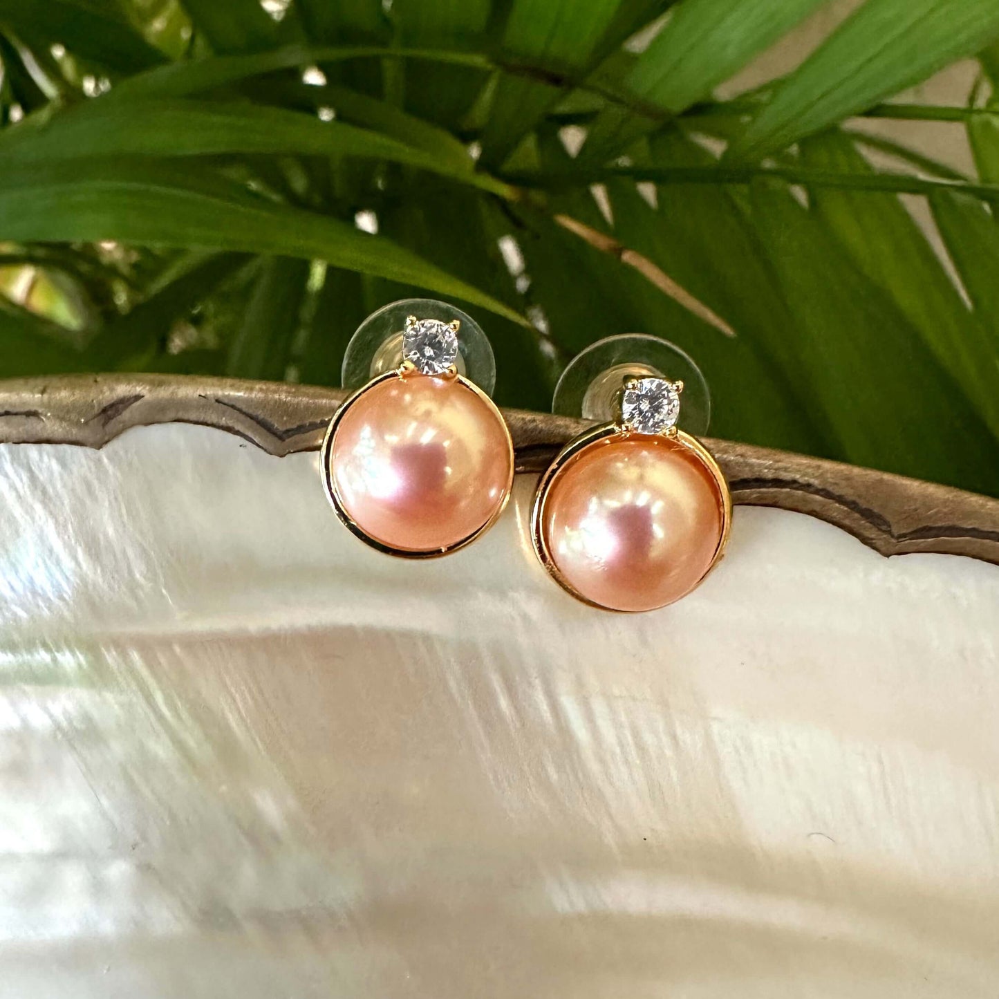 Close-up of Edison Mabe pearl stud earrings on white pearl shell with green leaf backdrop handmade in Canada