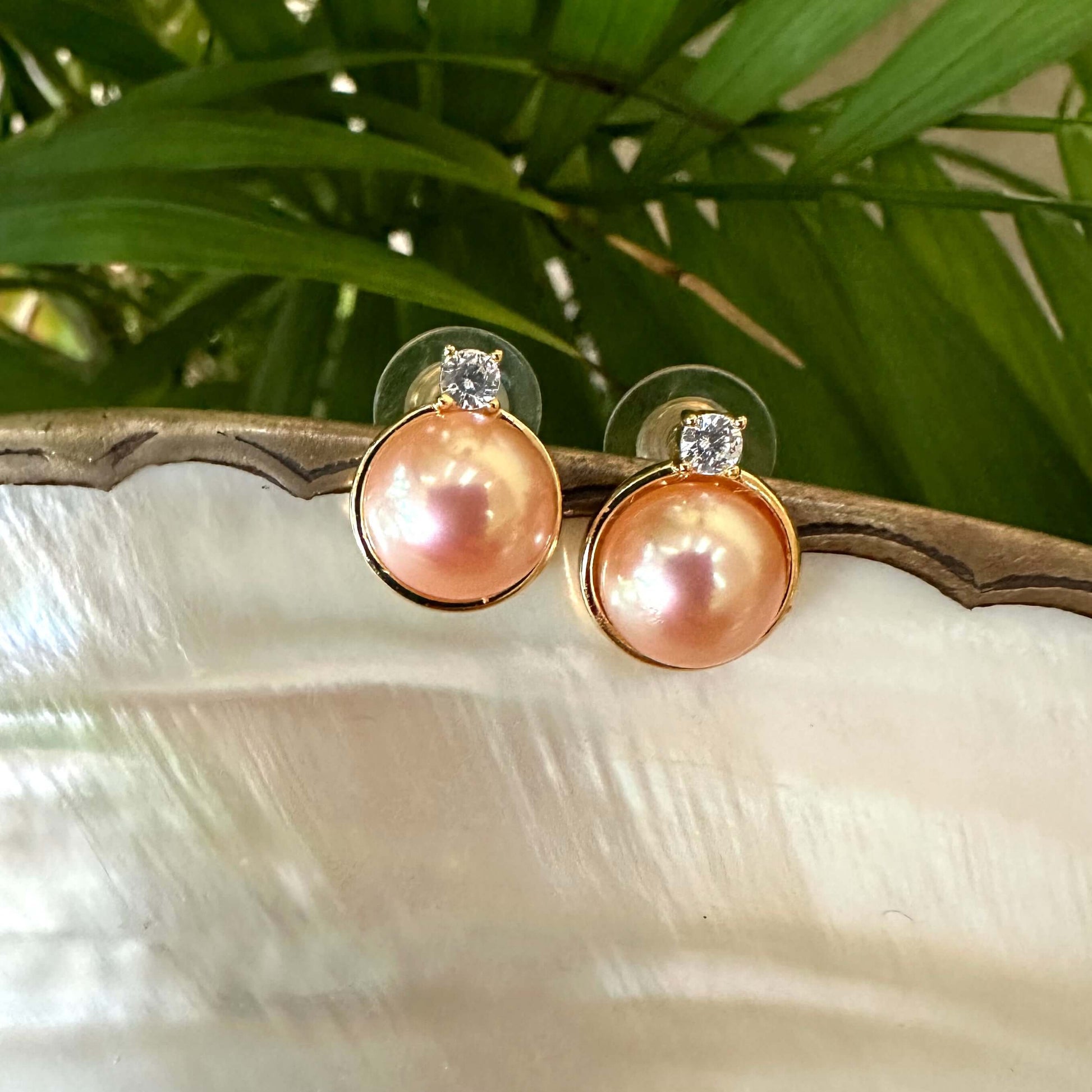 Close-up of Edison Mabe pearl stud earrings on white pearl shell with green leaf backdrop handmade in Canada