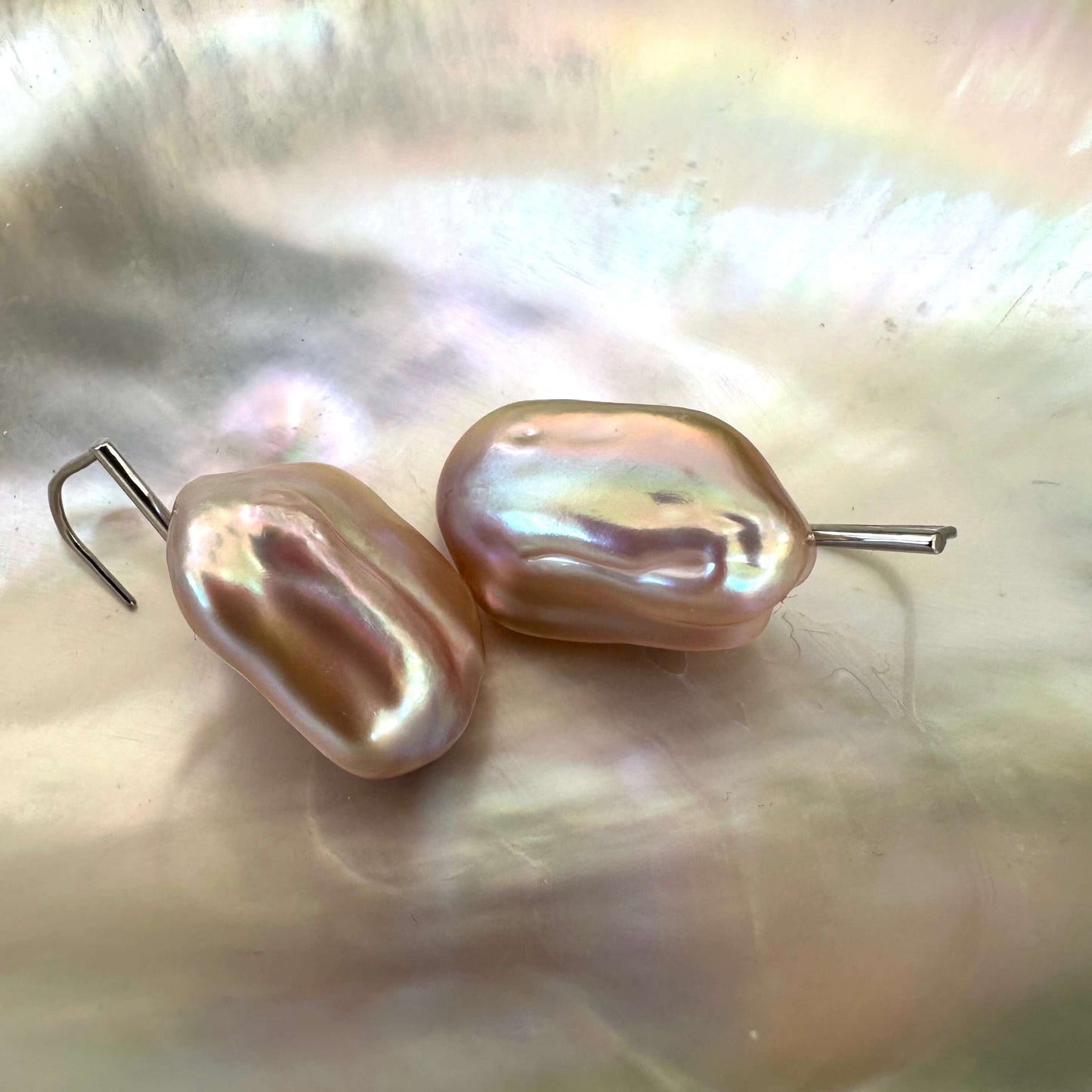 Elegant purple pearl drop earrings displayed on white shell, highlighting handcrafted silver hooks and lustrous baroque texture.