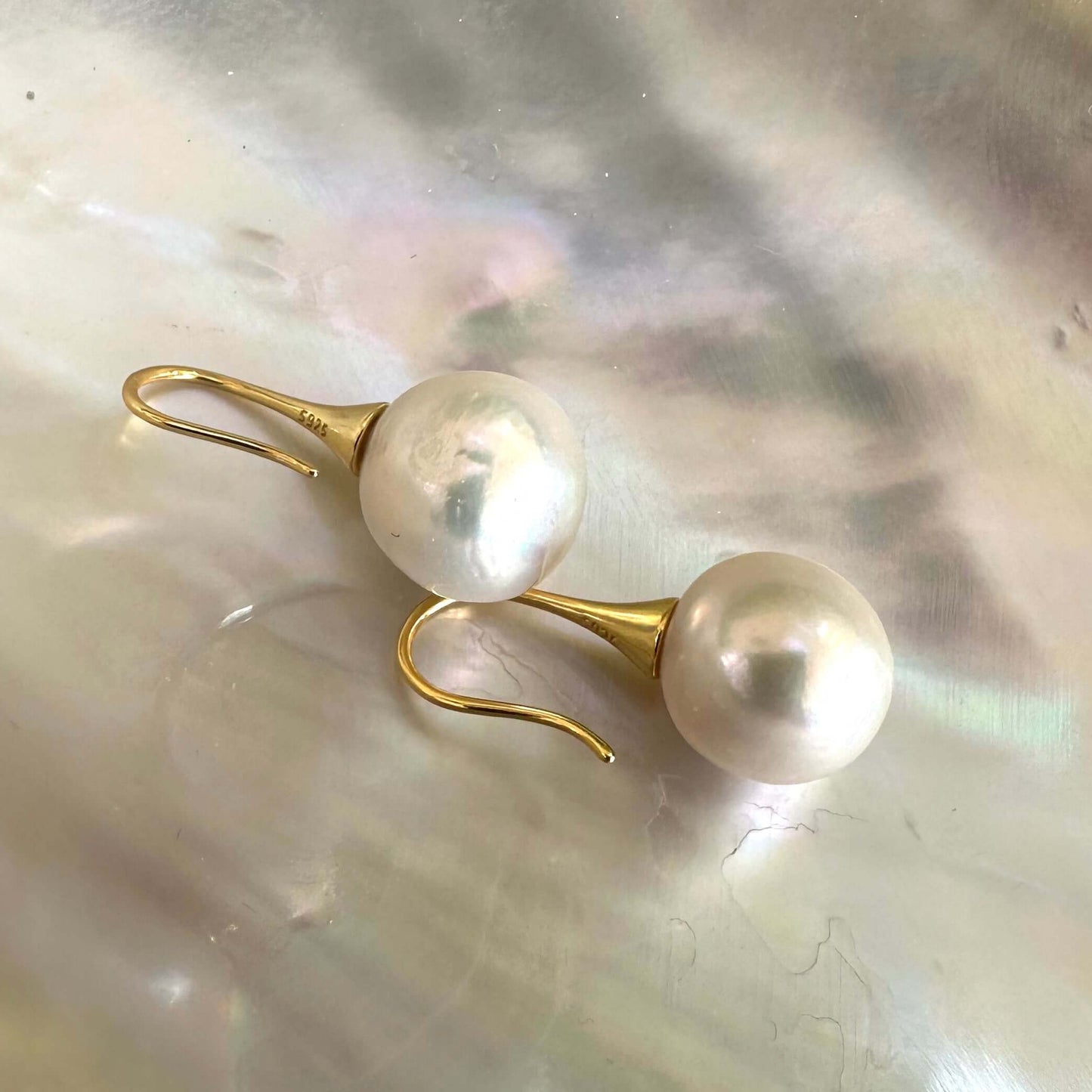 Large Edison white pearl drop earrings displayed on white shell, highlighting craftsmanship and delicate gold vermeil hooks.