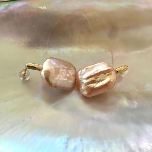 Golden peach pearl drop earrings shown on shell, capturing metallic peach tone and organic shape of large baroque freshwater pearls.
