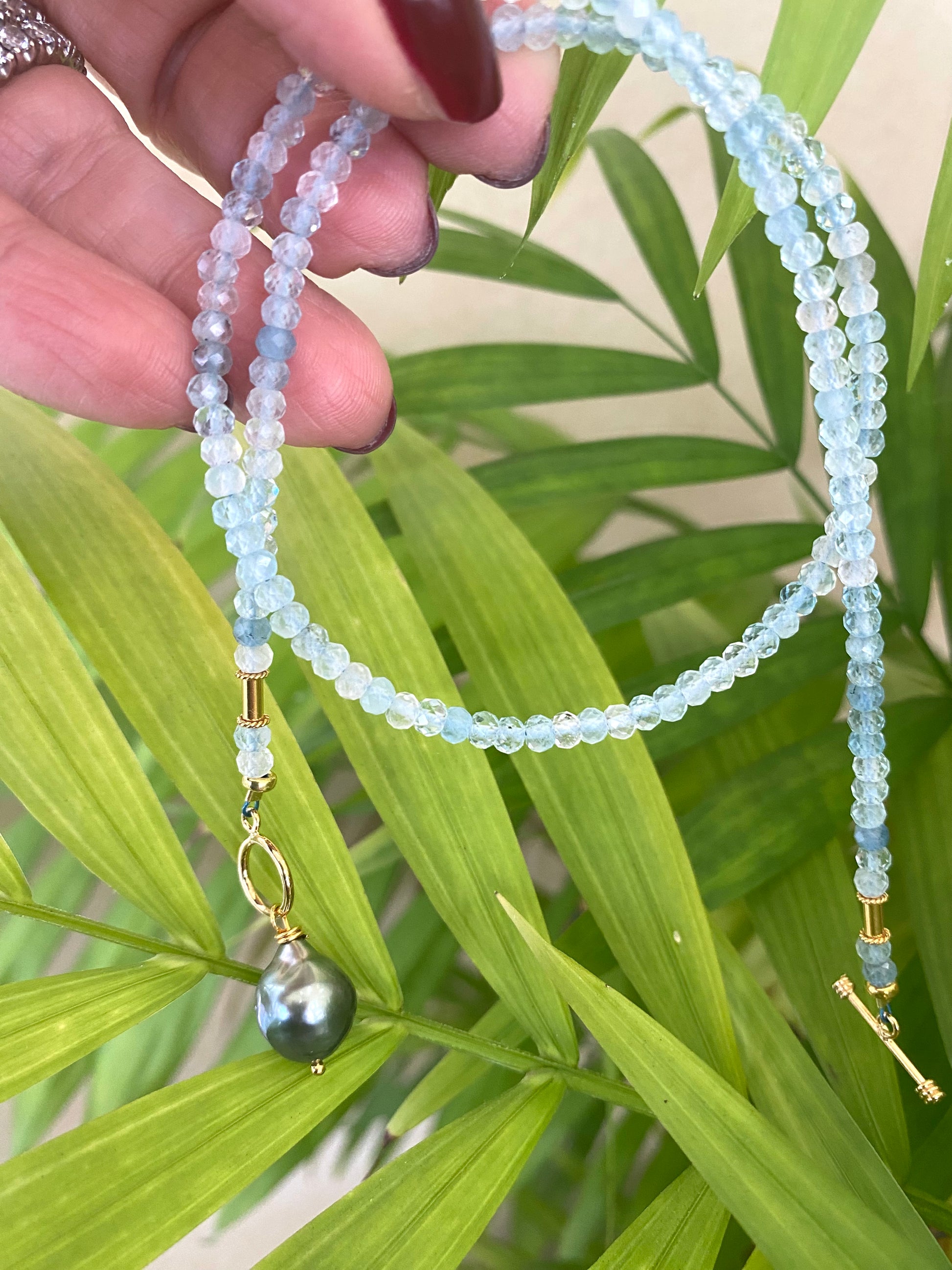 Aquamarine Pearl Pendant Necklace showcasing aquamarine rondelle beads and a Tahitian baroque pearl pendant on a green background.