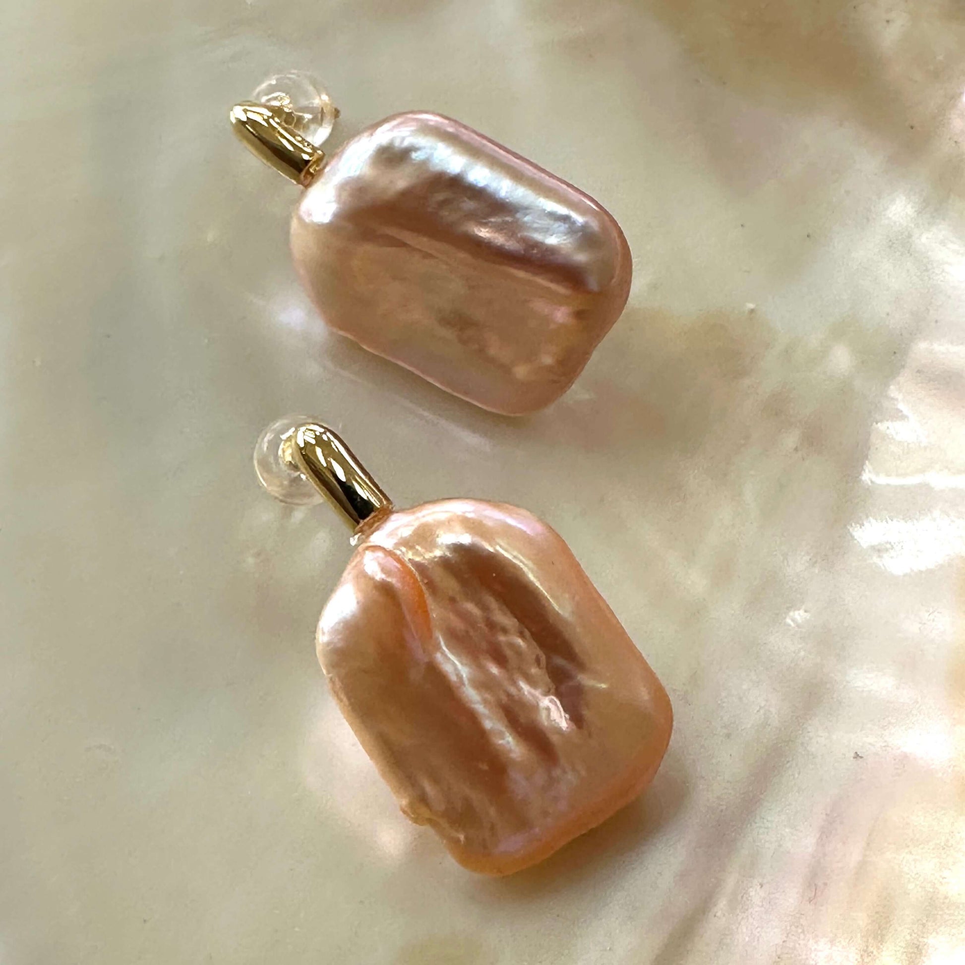 Golden peach pearl drop earrings with rectangular baroque pearls displayed on white shell, showing lustrous golden hue and texture.