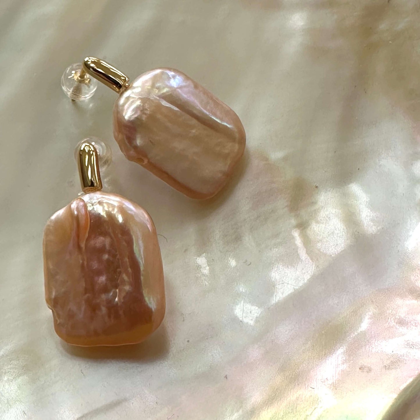 Golden peach pearl drop earrings with rectangular pearls displayed on shell, showing elegant handcrafted design and surface luster.