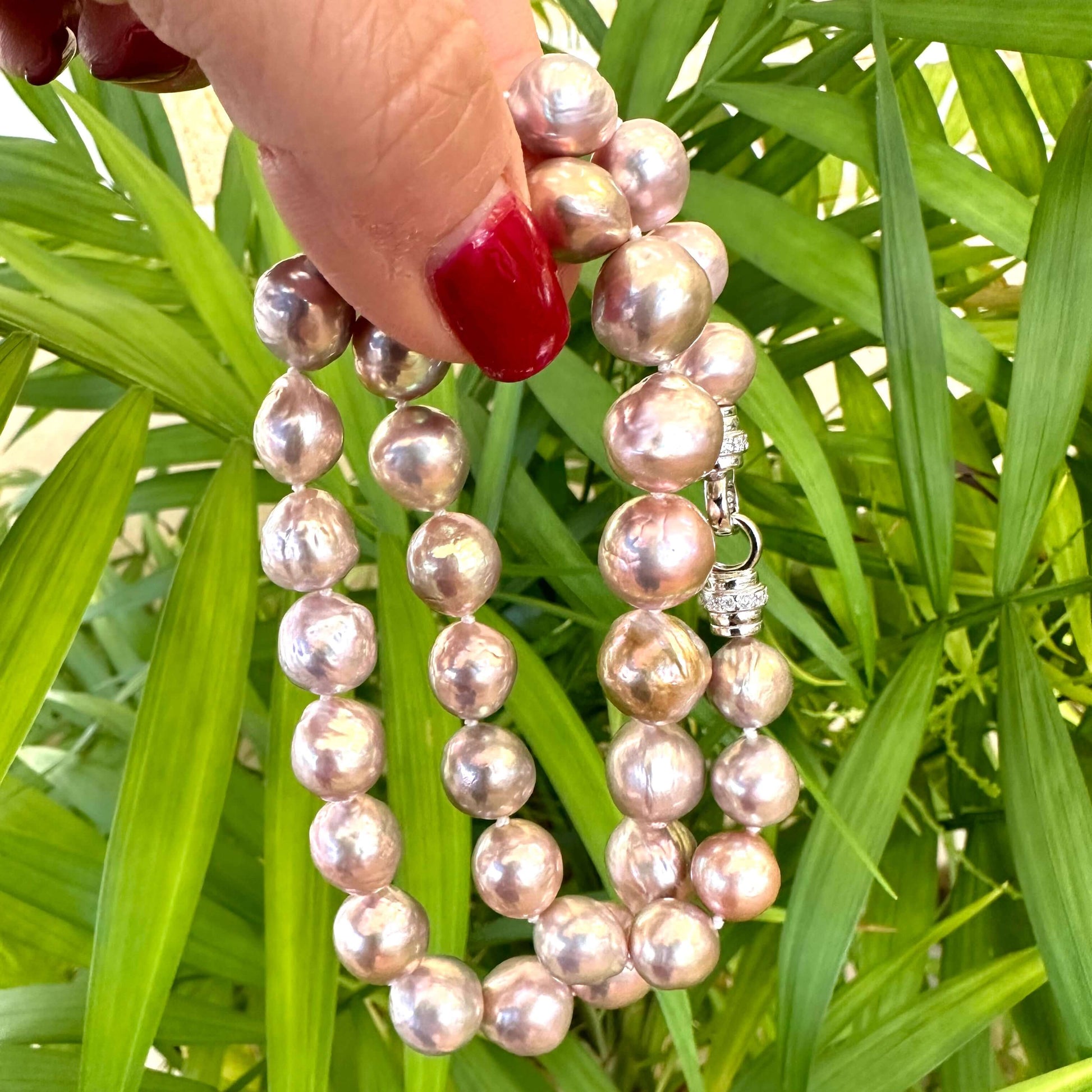 Hand holding pink lavender pearl necklace outdoors, highlighting soft iridescent tones and authentic baroque pearls.
