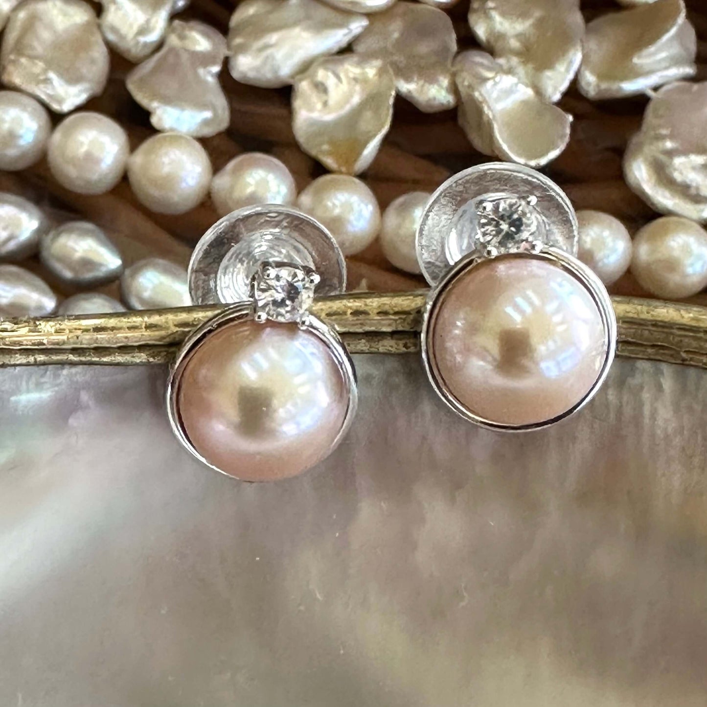 Pink mabe pearl stud earrings with CZ surrounded by assorted pearls on white shell, emphasizing size contrast and craftsmanship.