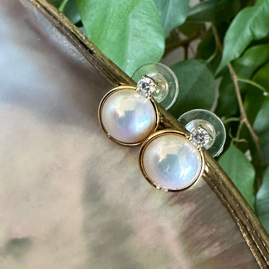 Mabe Edison pearl stud earrings in gold vermeil with CZ halo on white pearl and green leaf background