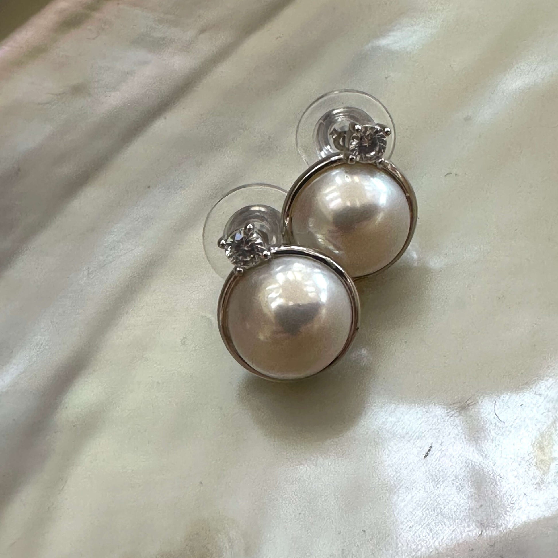 White mabe pearl stud earrings with CZ in sterling silver displayed on white pearl shell, showing soft luster and elegant design.